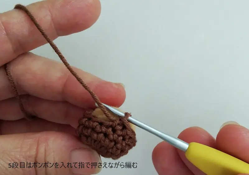 どんぐり本体の中にポンポンを入れて指で押さえながら5段目を編んでいる所