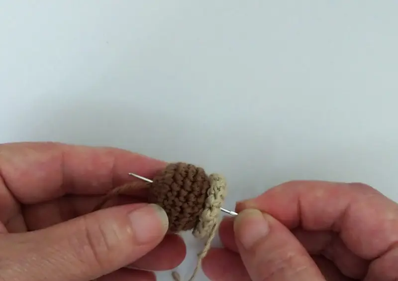 鎖編みの茎を作った糸をとじ針に通し、どんぐり本体のに向かってまっすぐ貫通させているところ